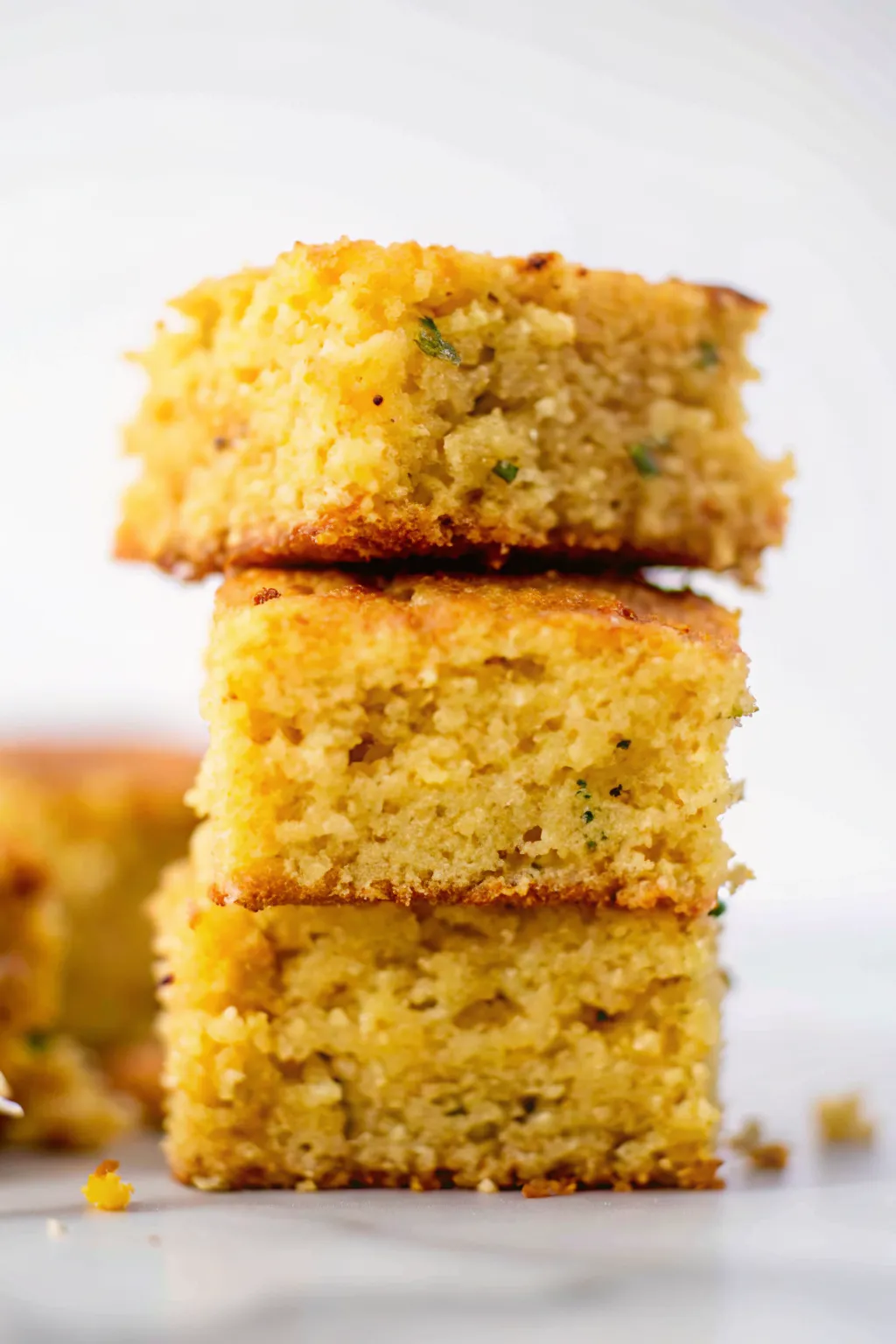 Three squares of jalapeño cornbread stacked on top of each other showing moist texture and flecks of green herbs